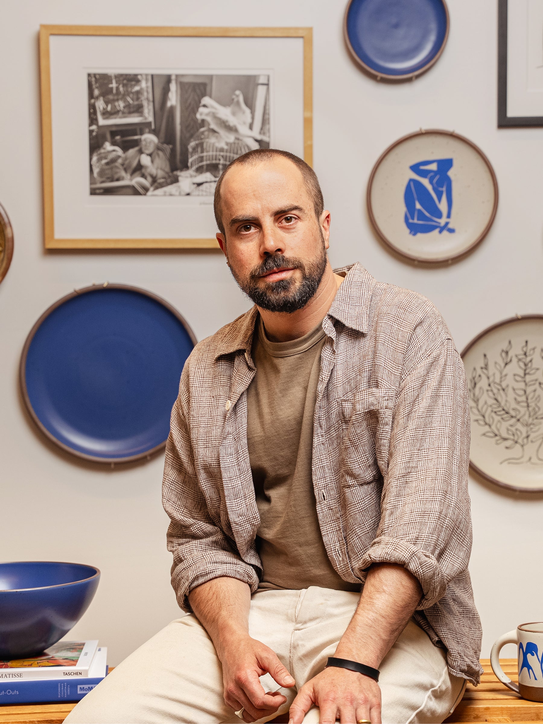 Alex Matisse staring at the camera with plates on the wall behind him from The Matisse Collection.