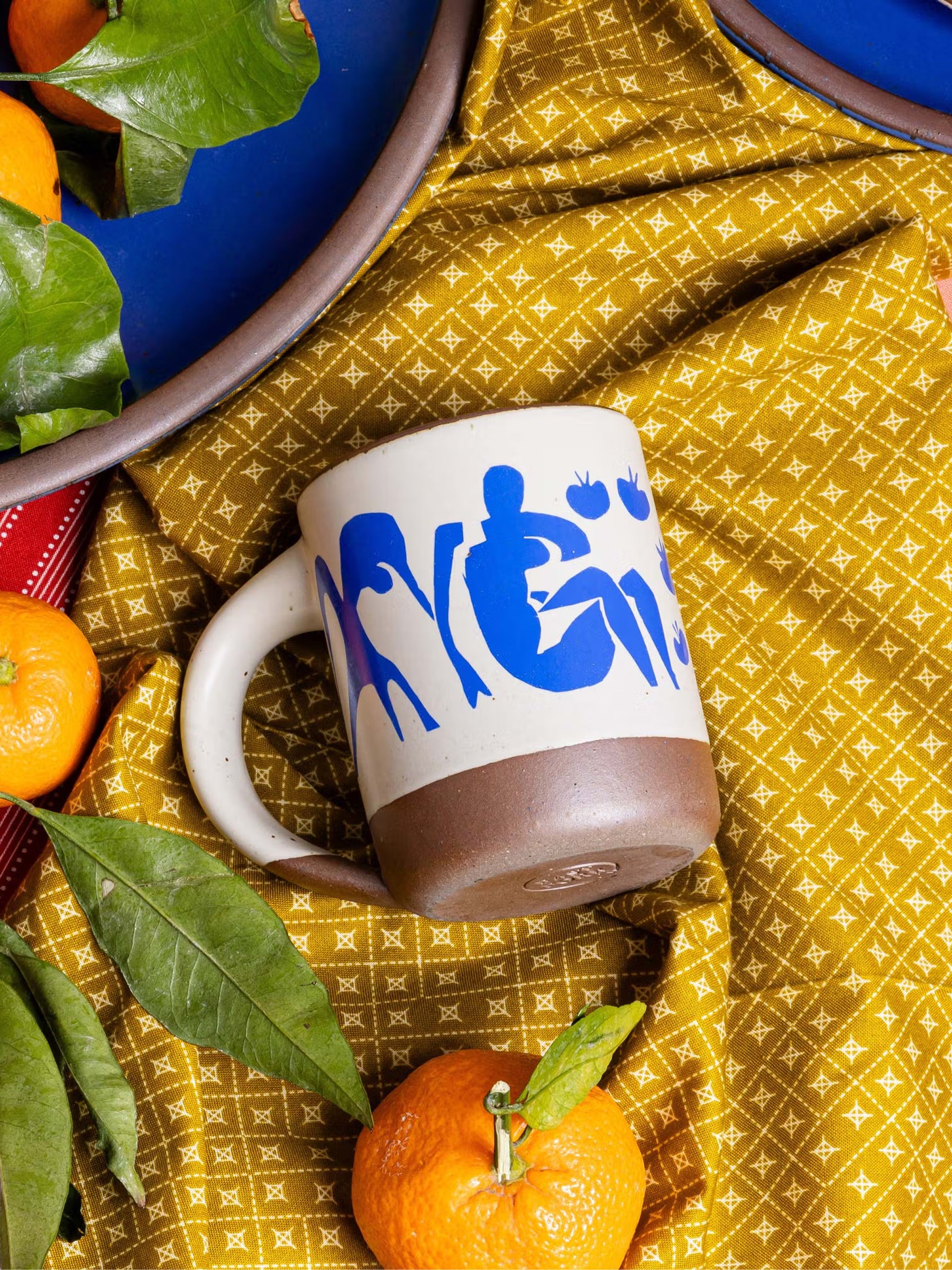 Femmes et singes mug on yellow fabric surrounded by oranges.
