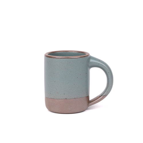 A medium sized ceramic mug with handle in a blue-grey color featuring iron speckles and unglazed rim and bottom base.
