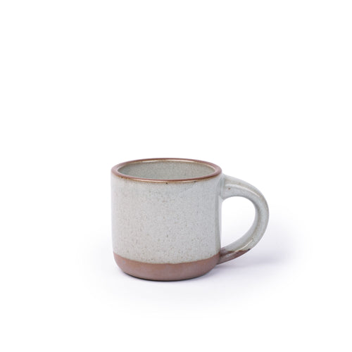 A small sized ceramic mug with handle in a reflective icy off-white featuring iron speckles and unglazed rim and bottom base.