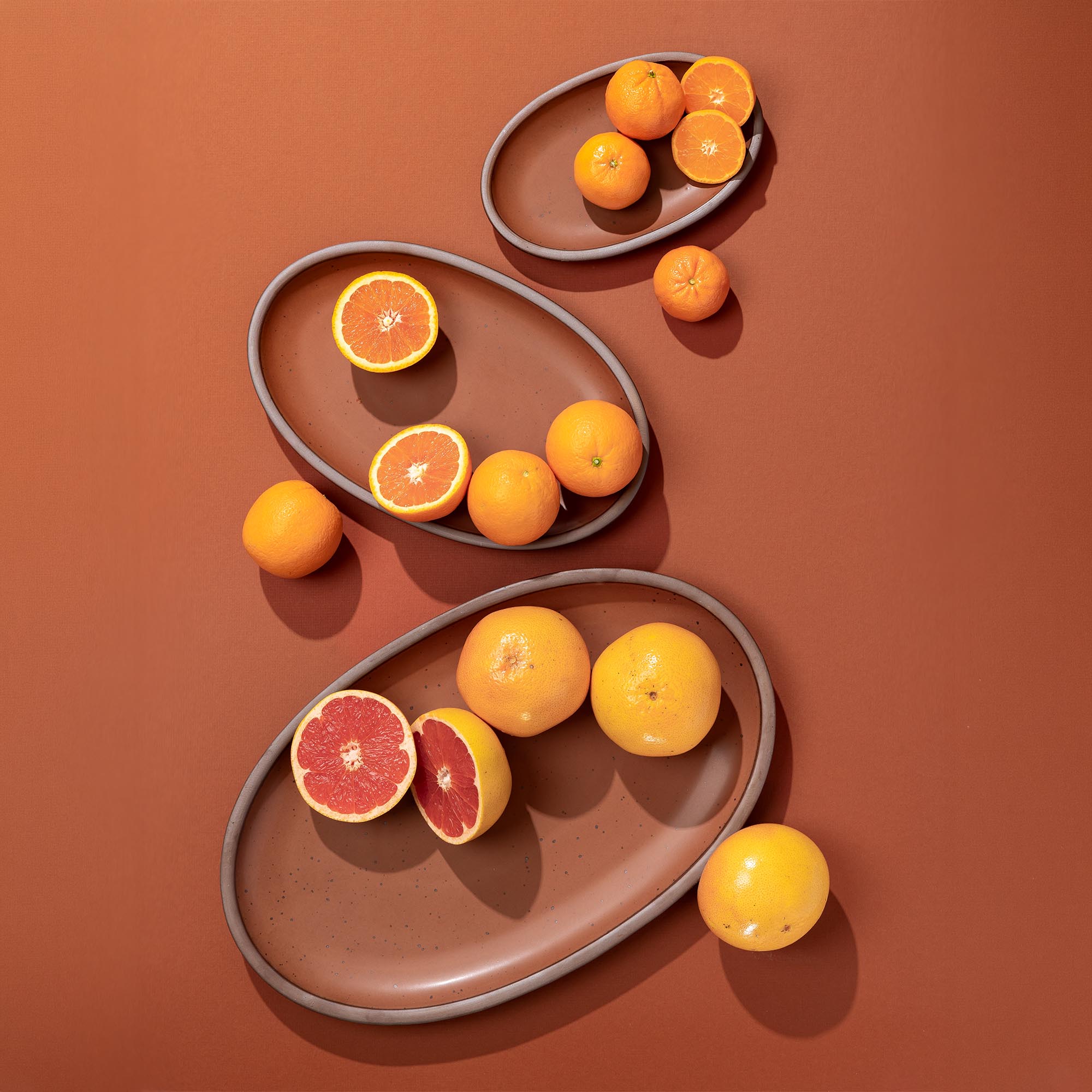 Oranges and grapefruits on cool terracotta platters in small medium and large against a matching background