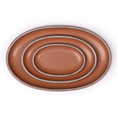 Set of three cool terracotta ceramic oval platters with unglazed rim nested together on a white background