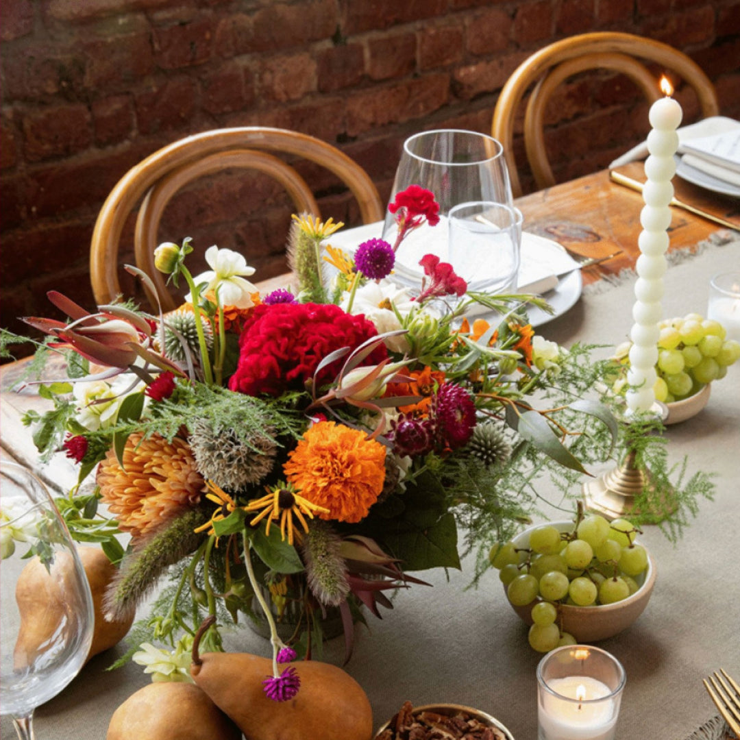 Decorative table setting with flowers, candles, and fruits against a brick wall.