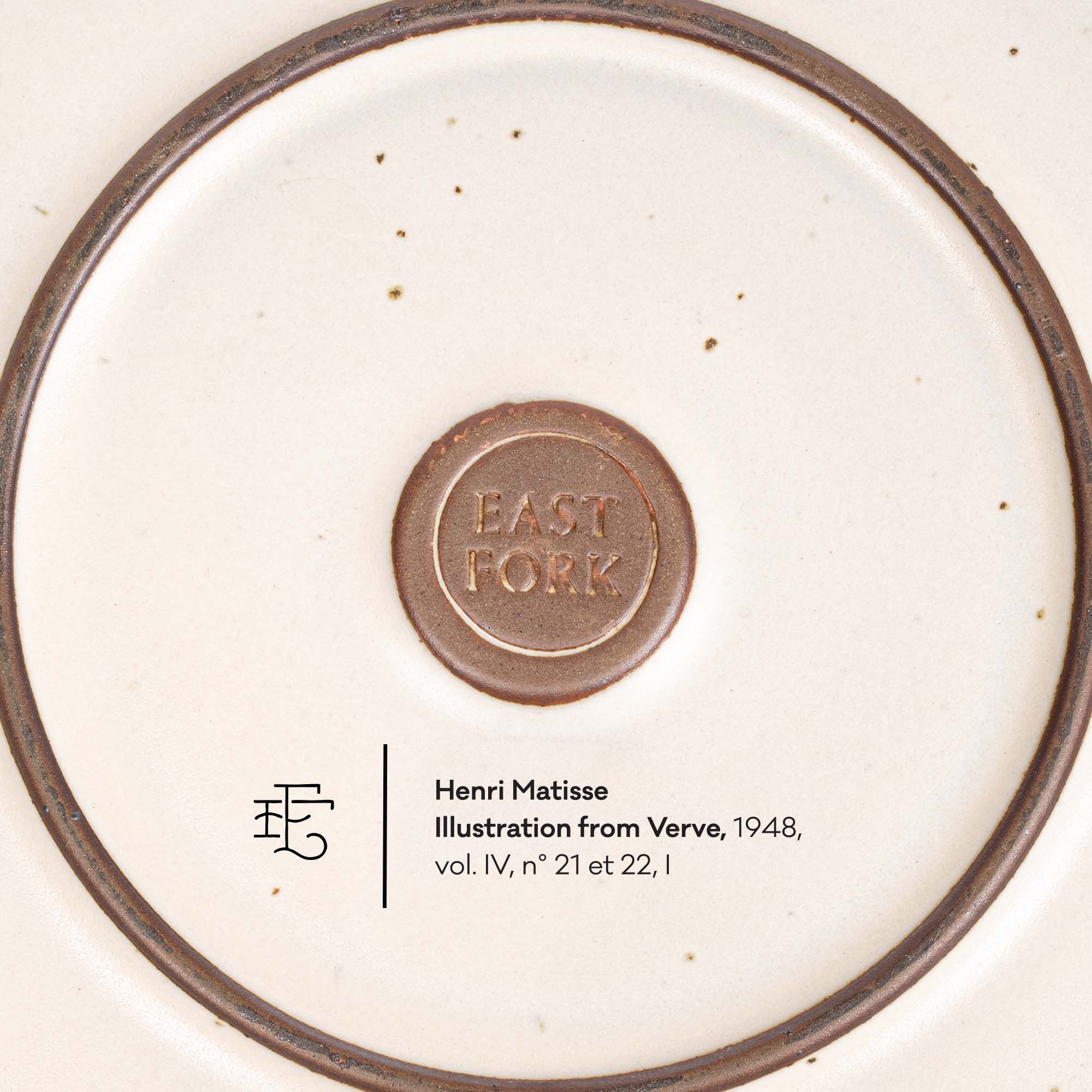 Close-up of the underside of a ceramic plate or dish, showing a cream-colored glaze with a dark brown rim, a central embossed brown seal reading 'EAST FORK,' and printed text below identifying Henri Matisse as the illustration from Verve, 1948.