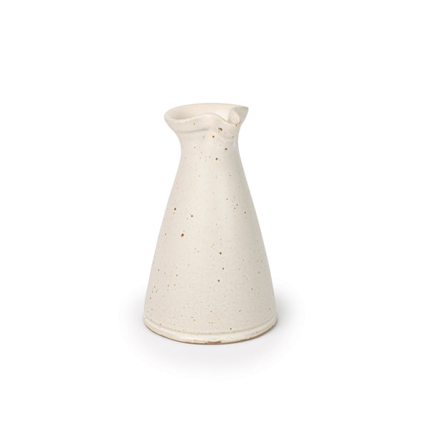 A small ceramic creamer with a narrow body and a subtle pouring spout at the top, in a warm off-white color, at an angle.