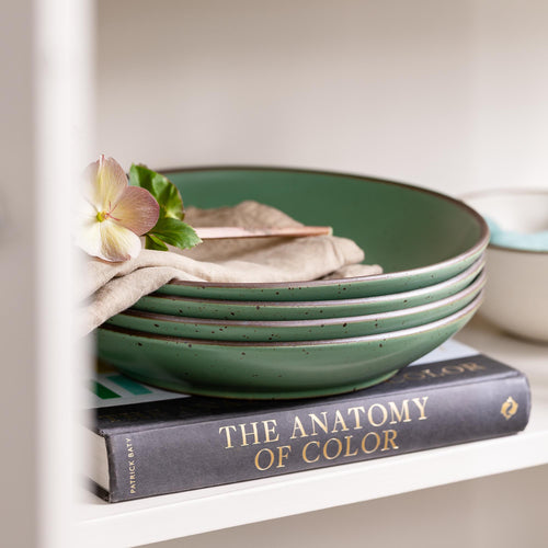 Stack of green ceramic bowls on a book titled 'The Anatomy of Color' with a flower and cloth.