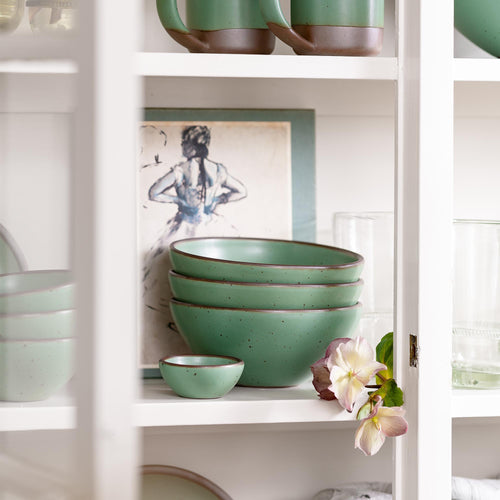 Stack of green ceramic bowls on a shelf with decorative elements.