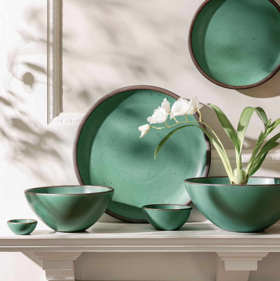 Set of green ceramic dishes on a table with white flowers.