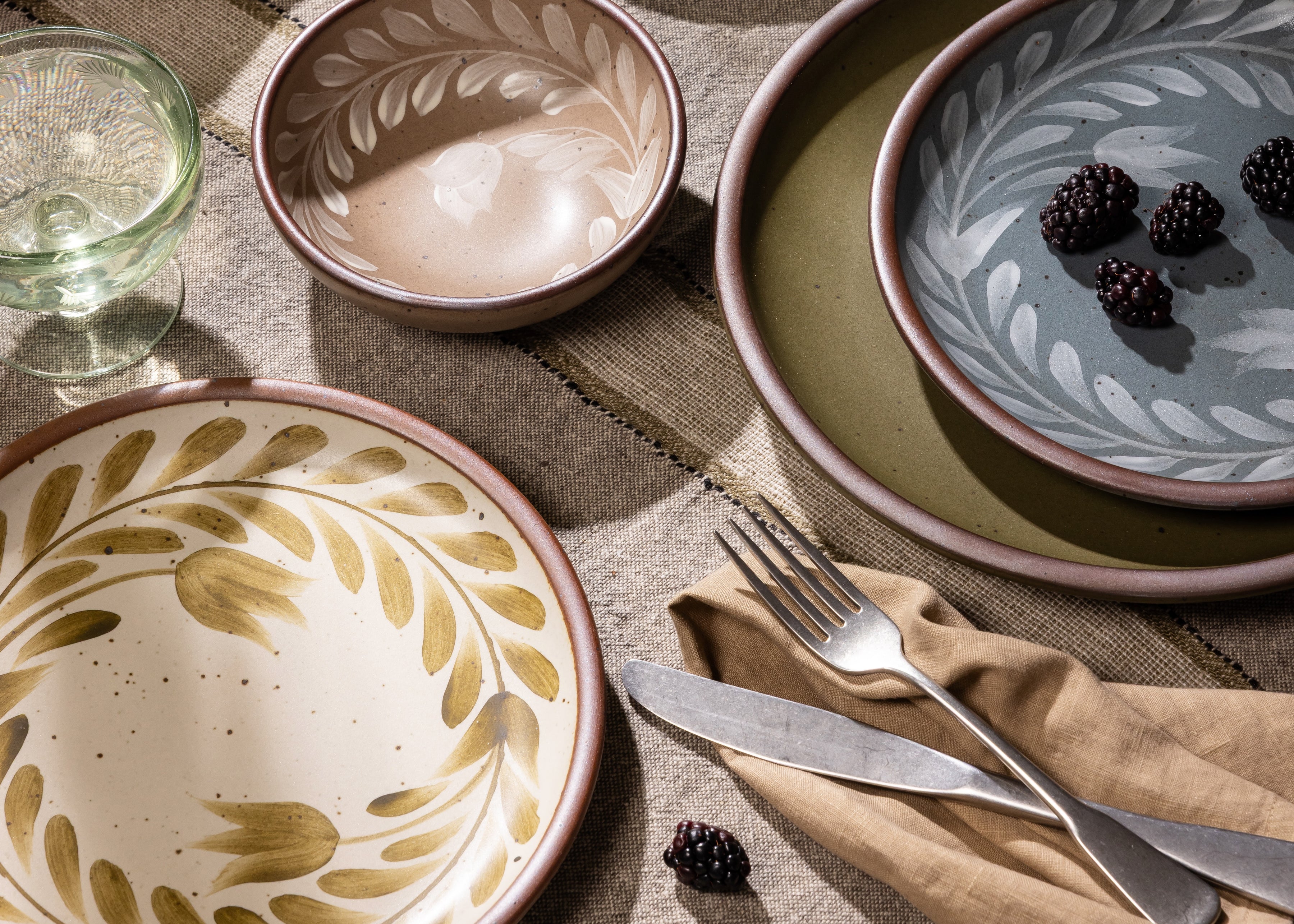 An overhead view of a table with hand painted dinnerware, silverware, napkin, and a coupe glass.