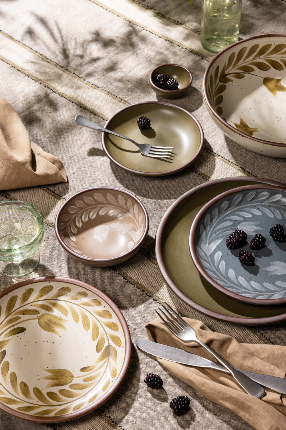 An overhead view of a table with hand painted dinnerware, silverware, napkin, and a coupe glass.