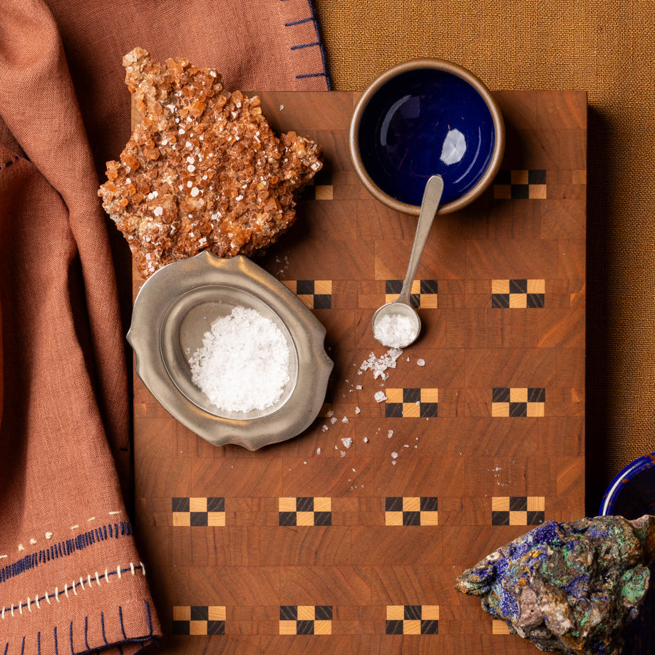 Quilted wooden cutting board with salt, ceramic dishes, 2 minerals arranged on rust-colored textiles.