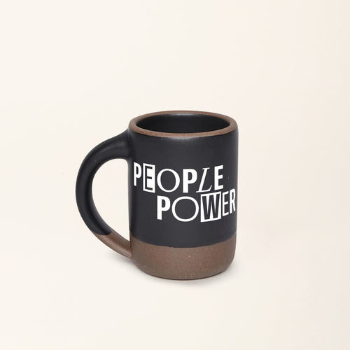A ceramic mug in a graphite black color with an unglazed base and rim, with a decal in white that reads 'PEOPLE POWER'