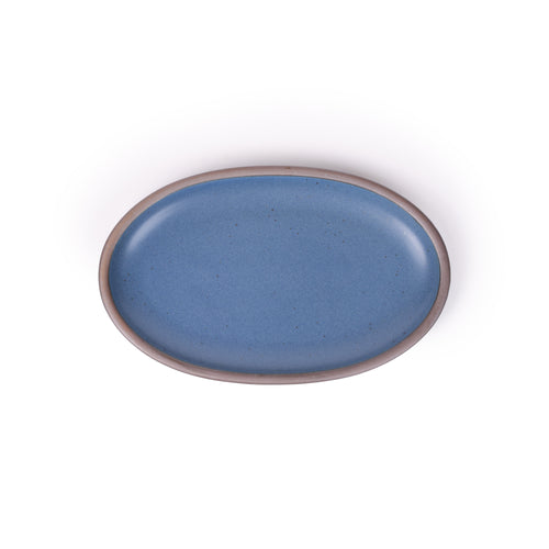 A medium oval ceramic platter in a blue color featuring iron speckles and an unglazed rim