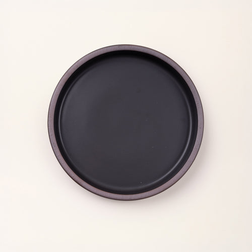 Overhead view of a shallow round ceramic baking dish in a matte graphite black color featuring an unglazed rim