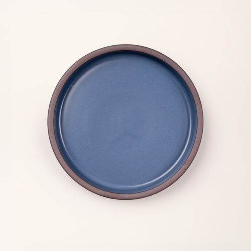 Overhead view of a shallow round ceramic baking dish in a grounded blue color featuring an unglazed rim