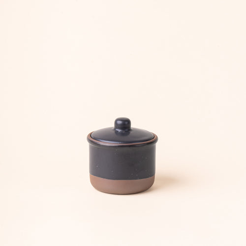 A short ceramic lidded jar in a graphic black color with an unglazed base.