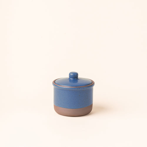 A short ceramic lidded jar in a grounded blue color with an unglazed base.
