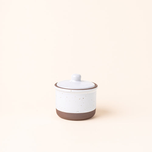 A short ceramic lidded jar in a cool white color with an unglazed base.