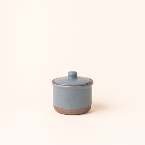 A short ceramic lidded jar in a blue-grey color with an unglazed base.