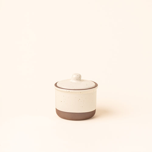 A short ceramic lidded jar in a warm off-white color with an unglazed base.