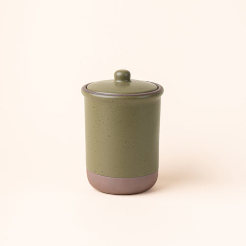 A tall ceramic lidded jar in an olive green color with an unglazed base.