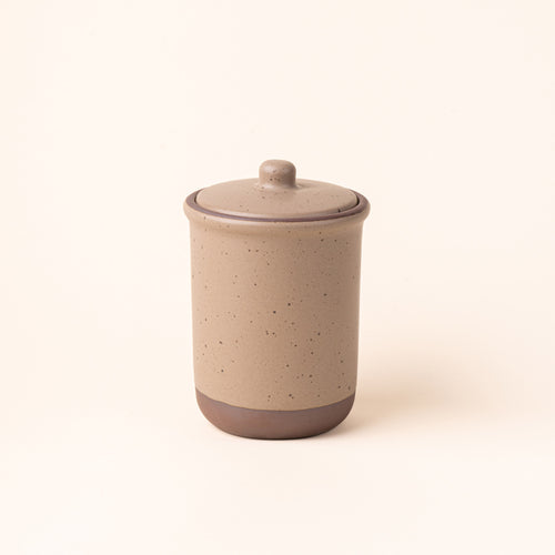 A tall ceramic lidded jar in a pale warm brown color with an unglazed base.