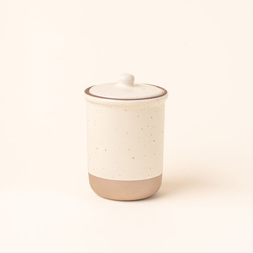 A tall ceramic lidded jar in a warm off-white color with an unglazed base.