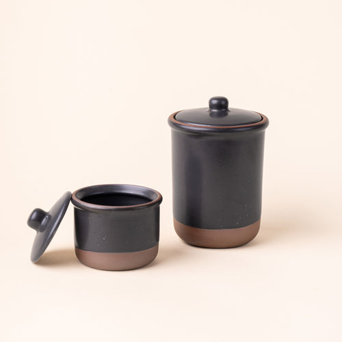 A small and tall ceramic lidded jars in a graphite black color with an unglazed base.