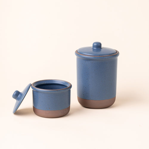 A small and tall ceramic lidded jars in a grounded blue color with an unglazed base.