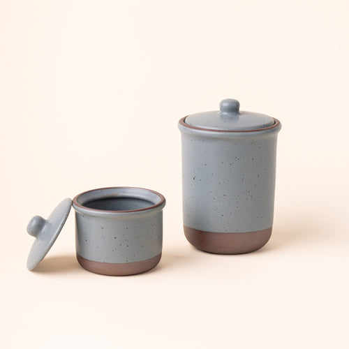 A small and tall ceramic lidded jars in a blue-grey color with an unglazed base.