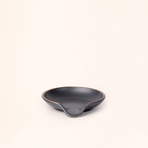 A ceramic spoon rest with a curved notch in a graphite black color with an unglazed rim.