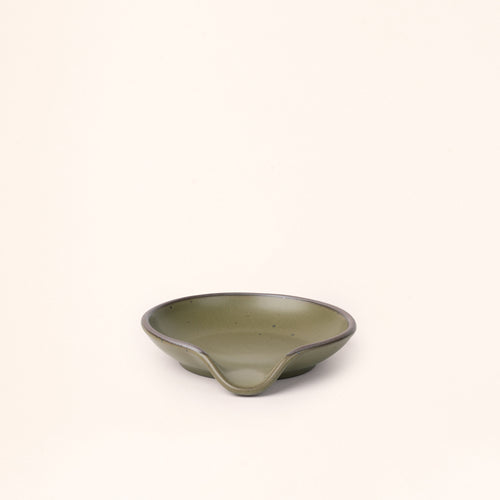 A ceramic spoon rest with a curved notch in an olive green color with an unglazed rim.