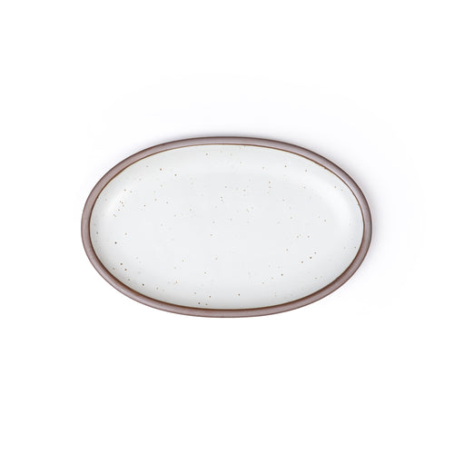 A medium oval ceramic platter in a cool white color featuring iron speckles and an unglazed rim