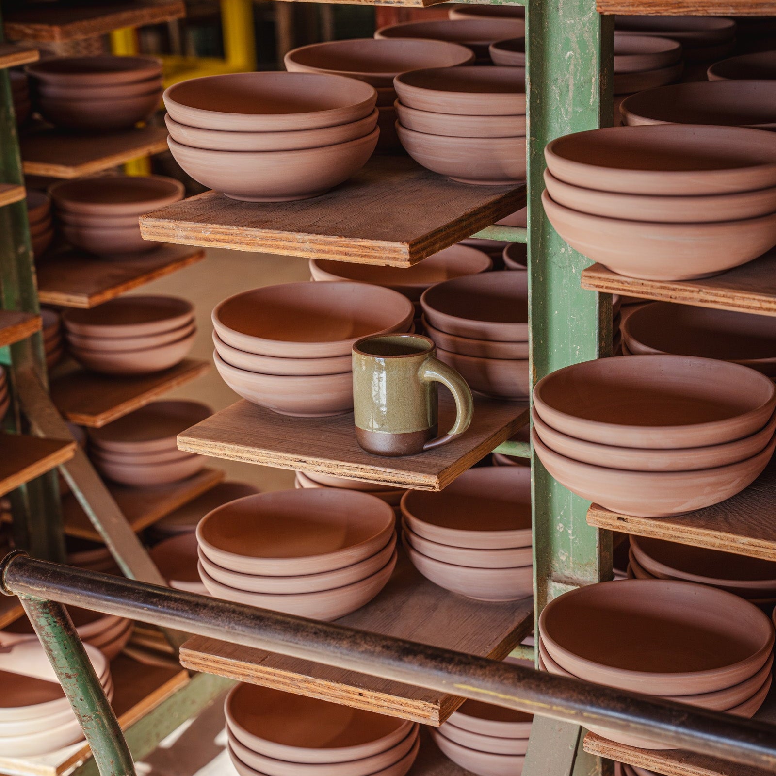 Inside a pottery factory with bowl bisqueware and a finished mug in a variegated green glossy glaze.