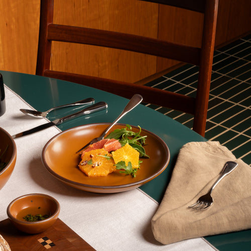 Earthy orange ceramic medium plate with a bowled edge with a fruit salad on a green table.