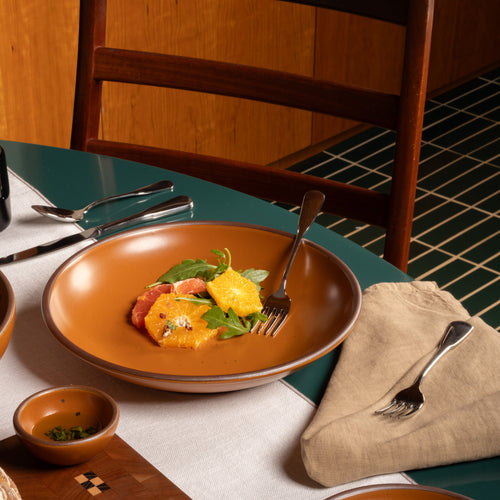Earthy orange ceramic large plate with a bowled edge with a fruit salad on a green table.