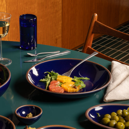 Glossy dark blue ceramic large plate with a bowled edge with a fruit salad on a green table.