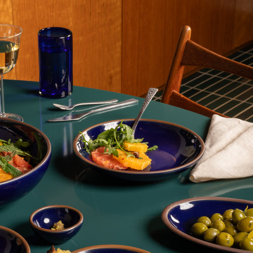 Glossy dark blue ceramic medium plate with a bowled edge with a fruit salad on a green table.