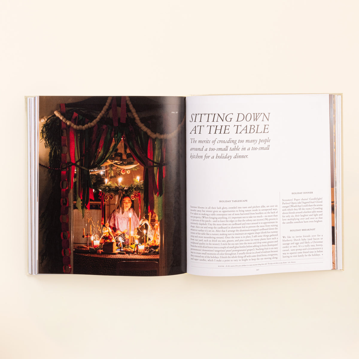 Open hardcover book showing a candlelit holiday table on the left page and a chapter titled “Sitting Down at the Table” on the right.