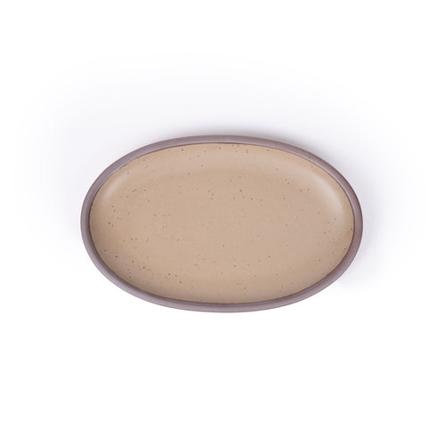 A medium oval ceramic platter in a pale warm brown color featuring iron speckles and an unglazed rim