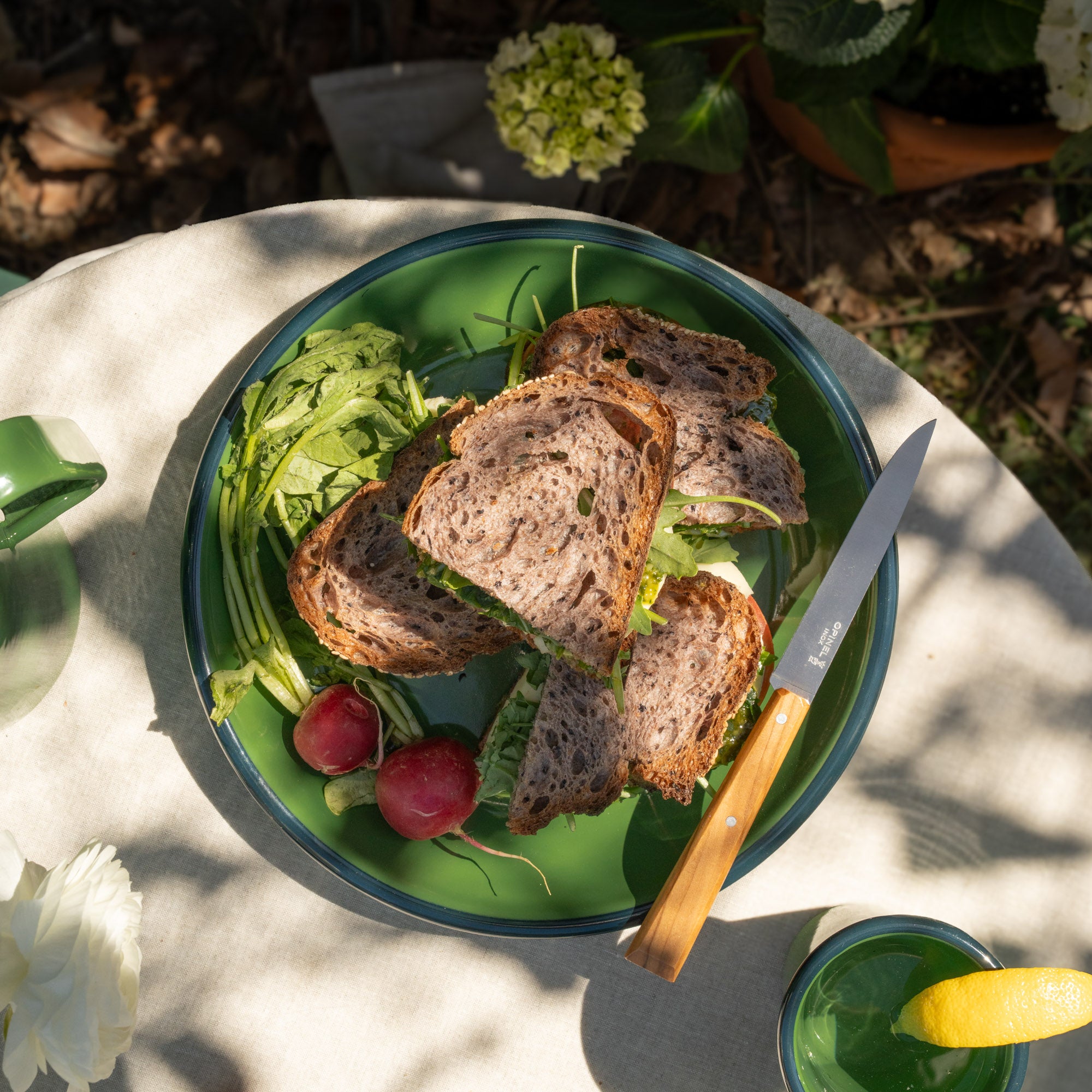 Green enamel dinner plate with sliced bread, salad, and a knife on a natural outdoor setting
