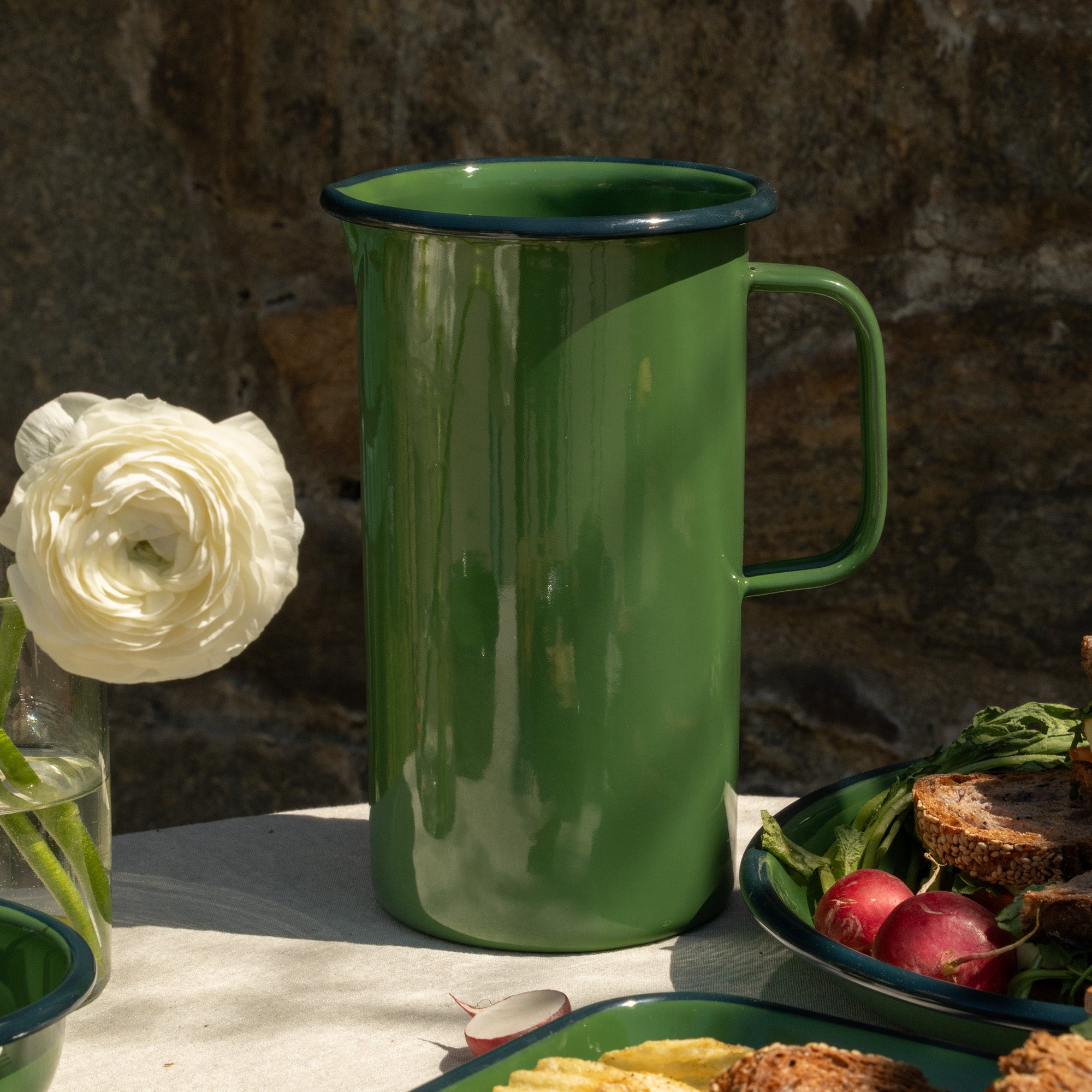 Green enamel pitcher on a table with food and a flower in the background