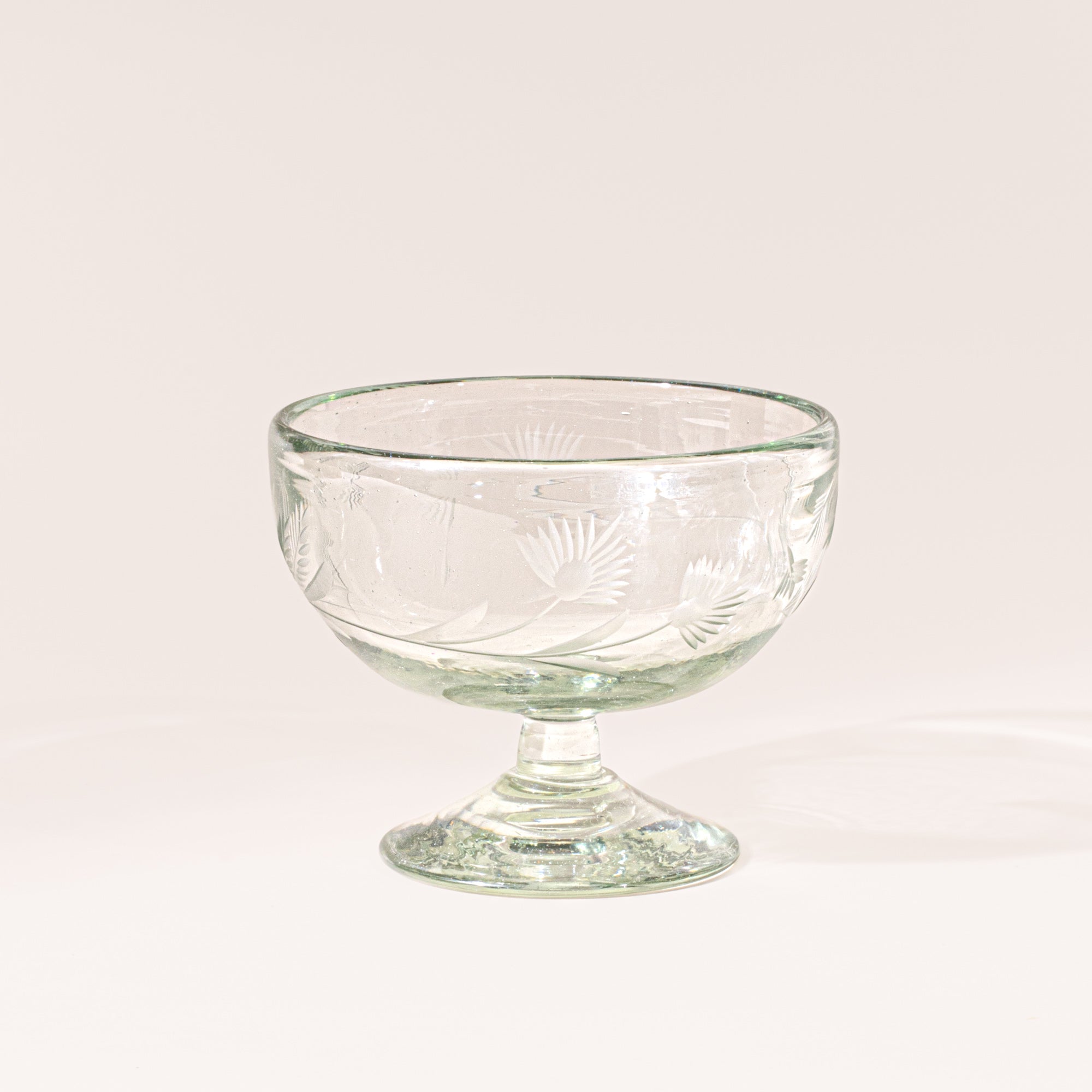 Clear etched coupe glass with a pedestal base and delicate botanical pattern, shown on a clean neutral background.