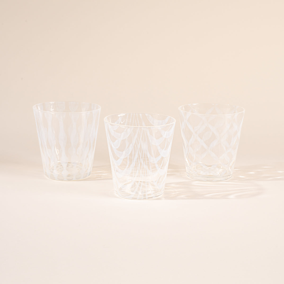 Three glasses half filled with delicate patterns and cascading shadows