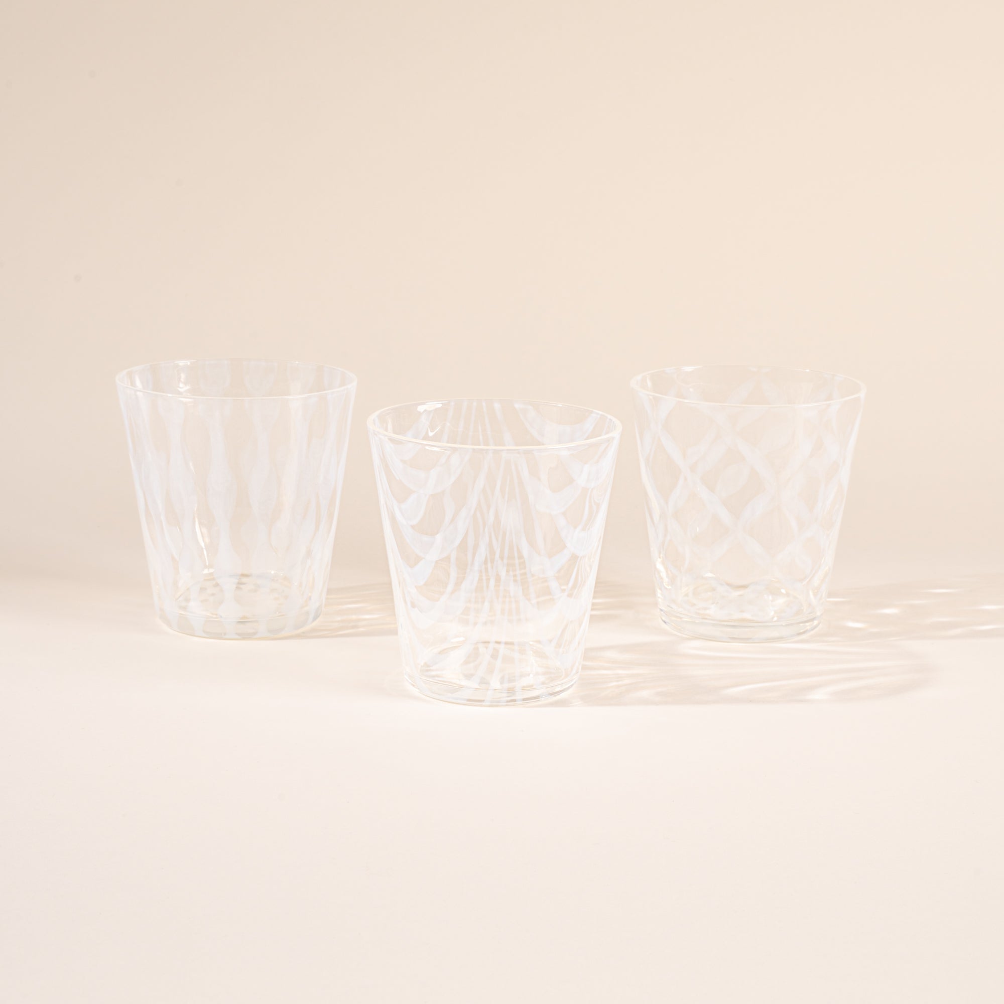 Three glasses half filled with delicate patterns and cascading shadows