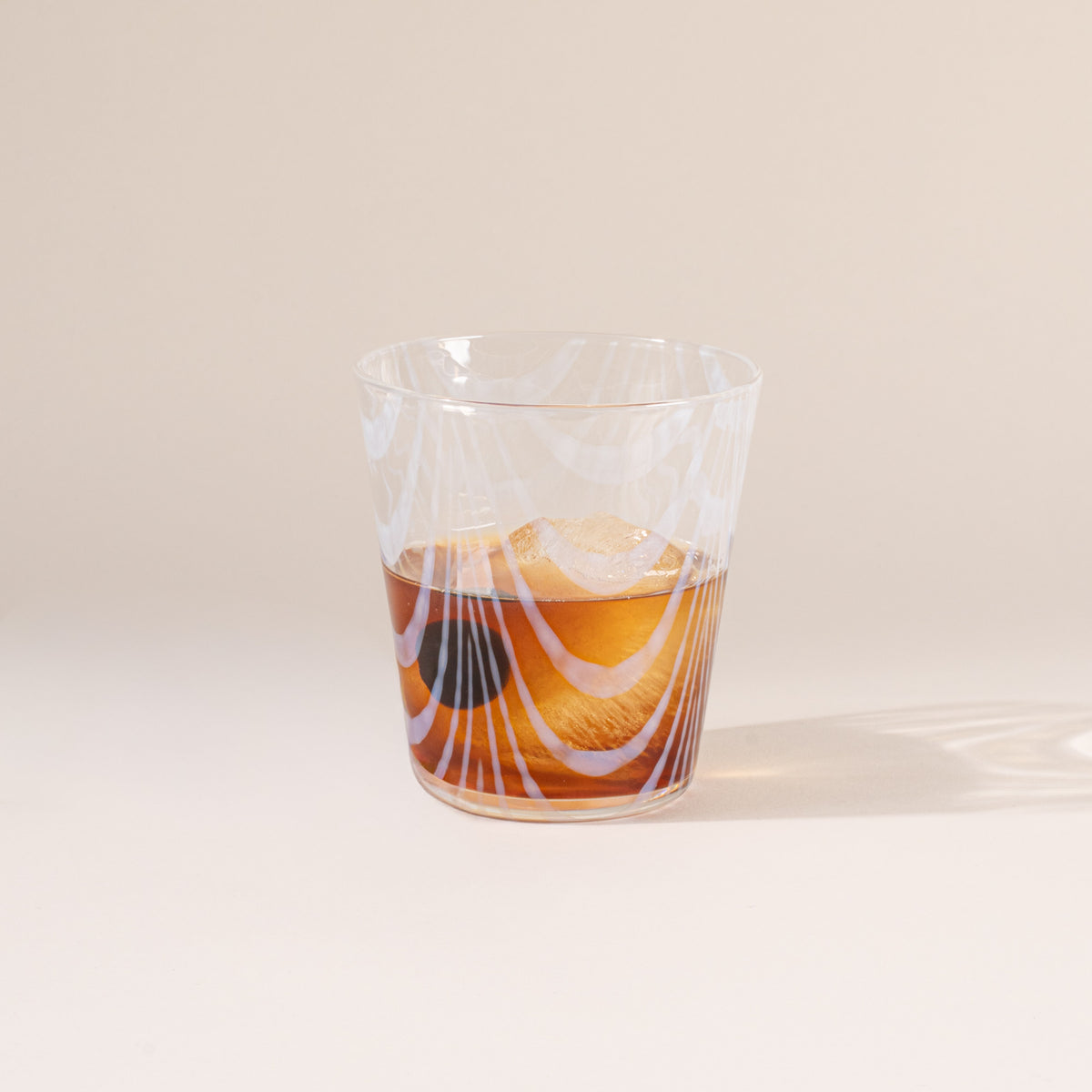 A short clear glass with a delicate ripple pattern, half filled with a drink
