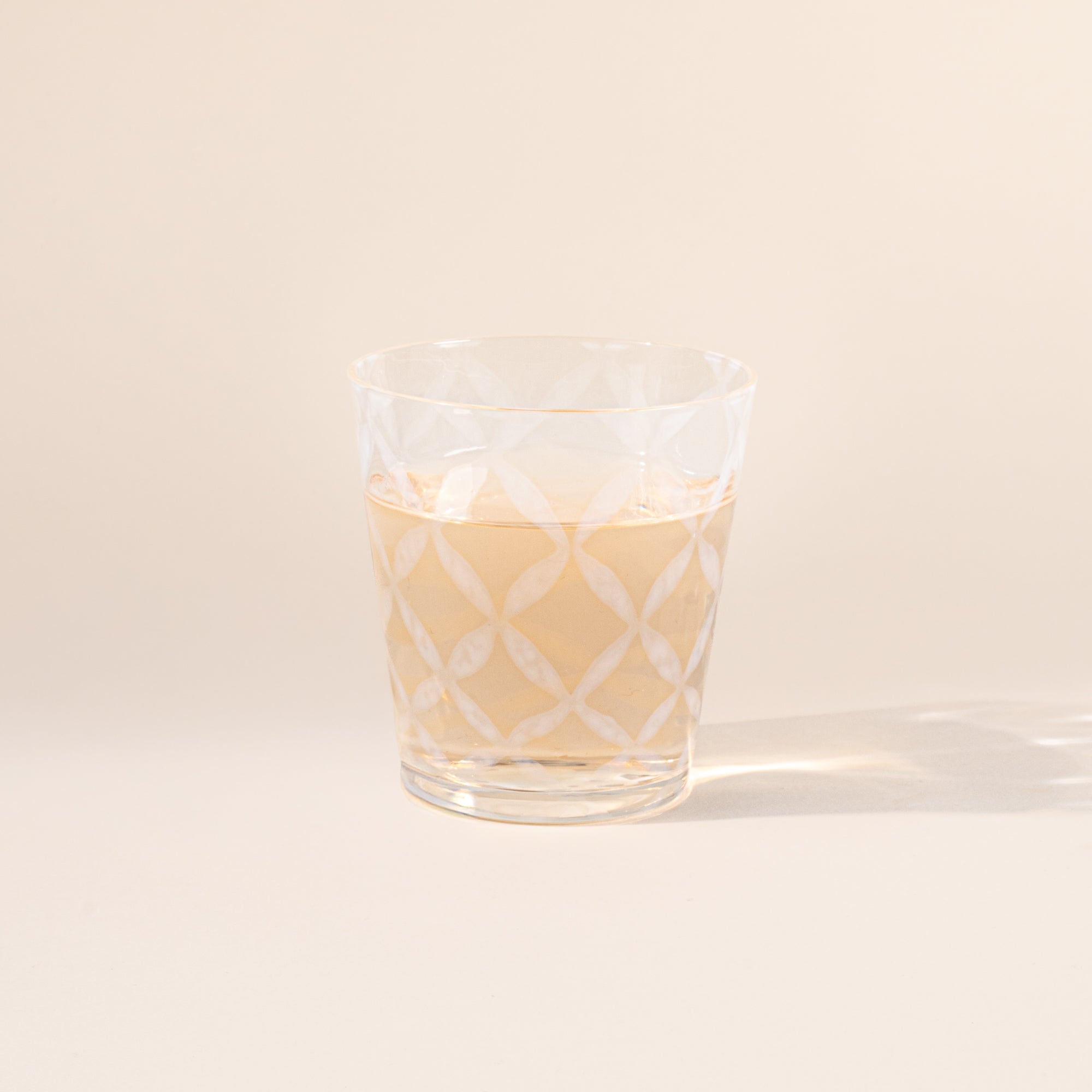 A short clear glass with a delicate grid pattern, half filled with a drink