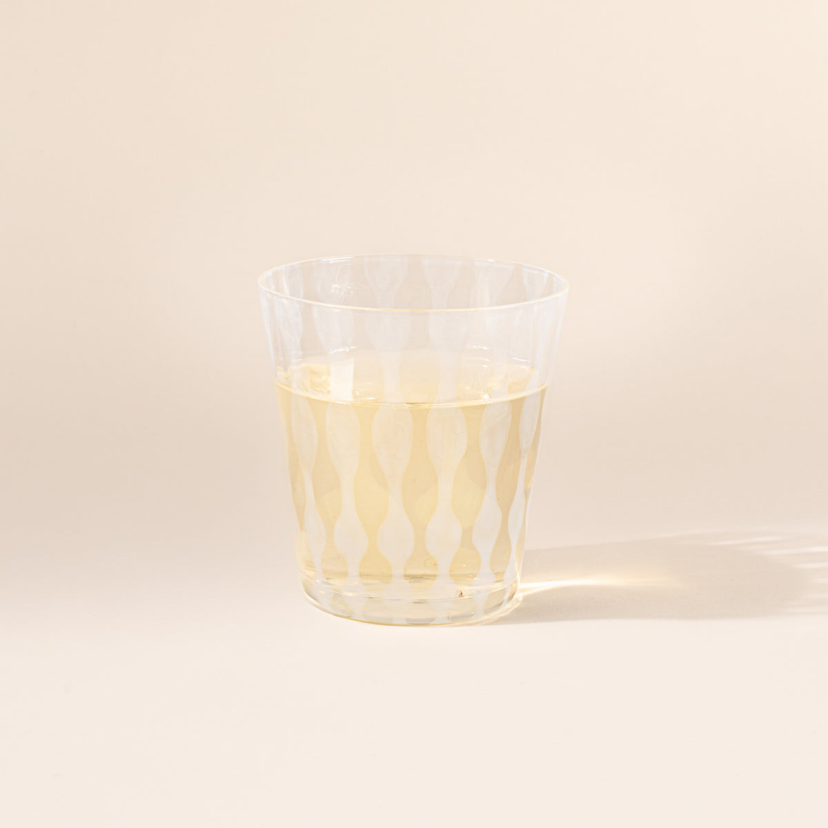 A short clear glass with a delicate vertical wave pattern, half filled with a drink