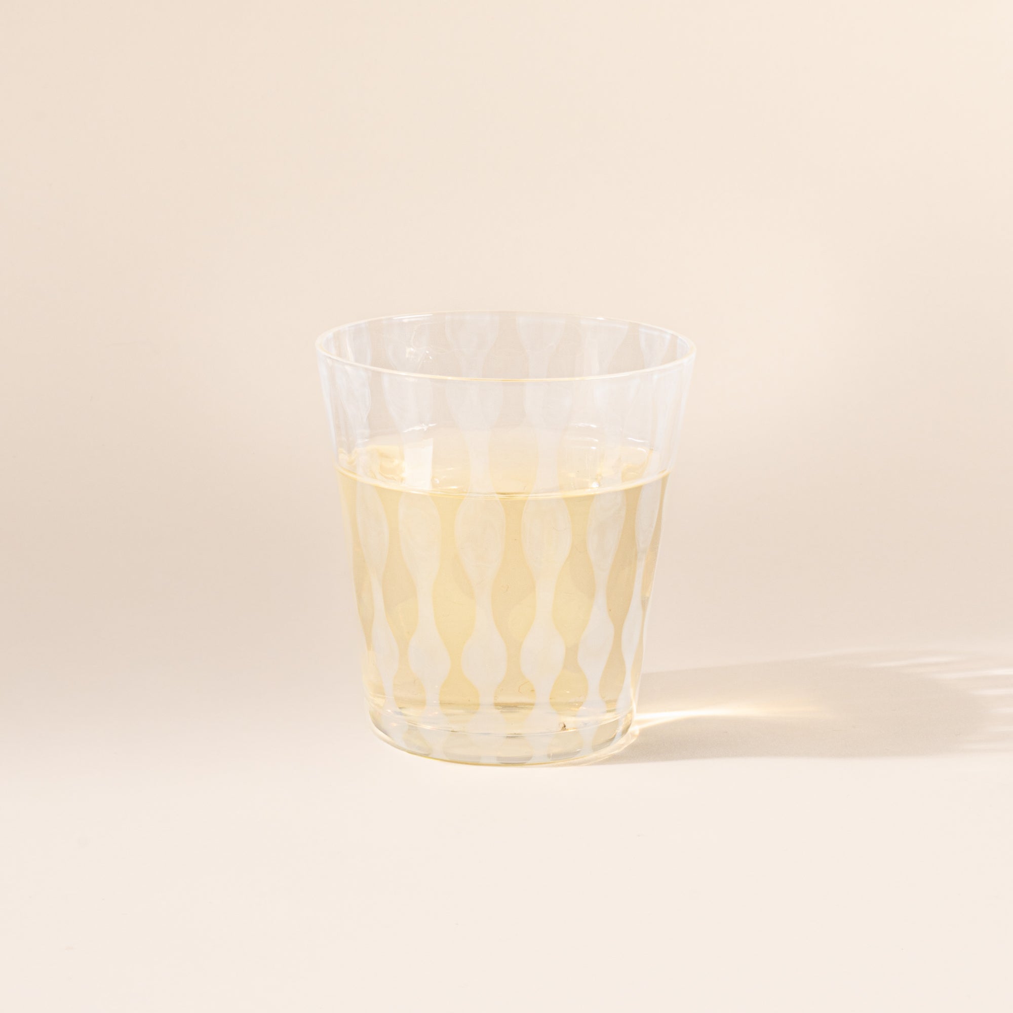 A short clear glass with a delicate vertical wave pattern, half filled with a drink