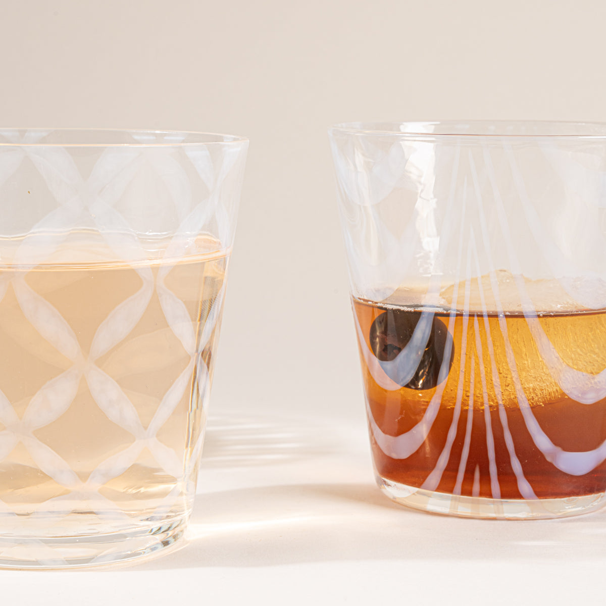 Two glasses half filled with delicate patterns and cascading shadows, filled with drinks